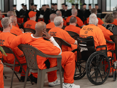 Future CIU Prison Initiative cohorts (in orange) watch the graduation ceremony with the current graduates in the background wearing their caps and gowns. (Photo by Noah Allard)