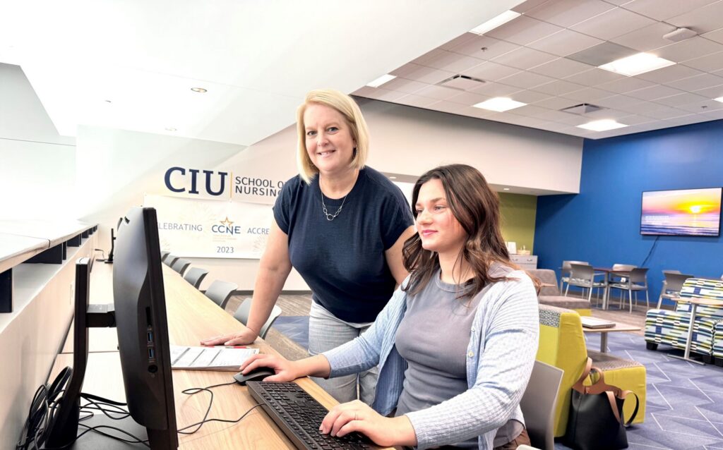 An academic advisor stands beside a student seated at a computer in the CIU School of Nursing building