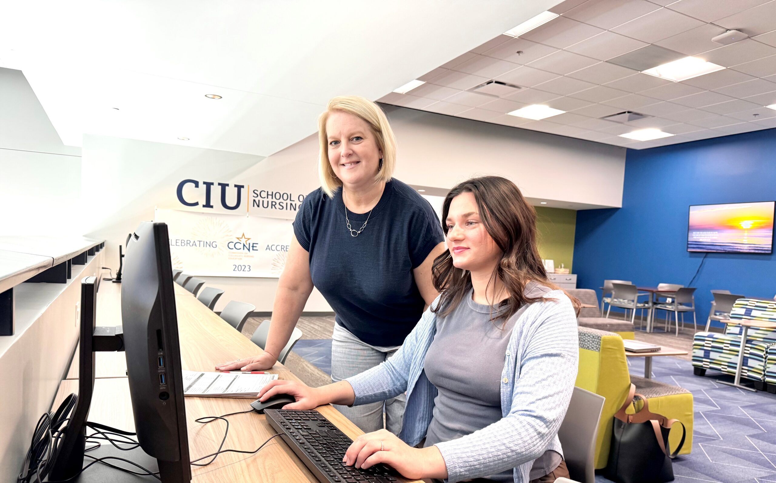 An academic advisor stands beside a student seated at a computer in the CIU School of Nursing building