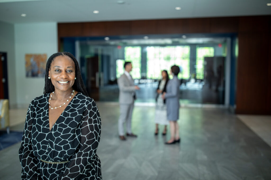 Dr. Tracy Miller smiling in the lobby of the William H. Jones Building at Columbia International University, with colleagues talking in the background
