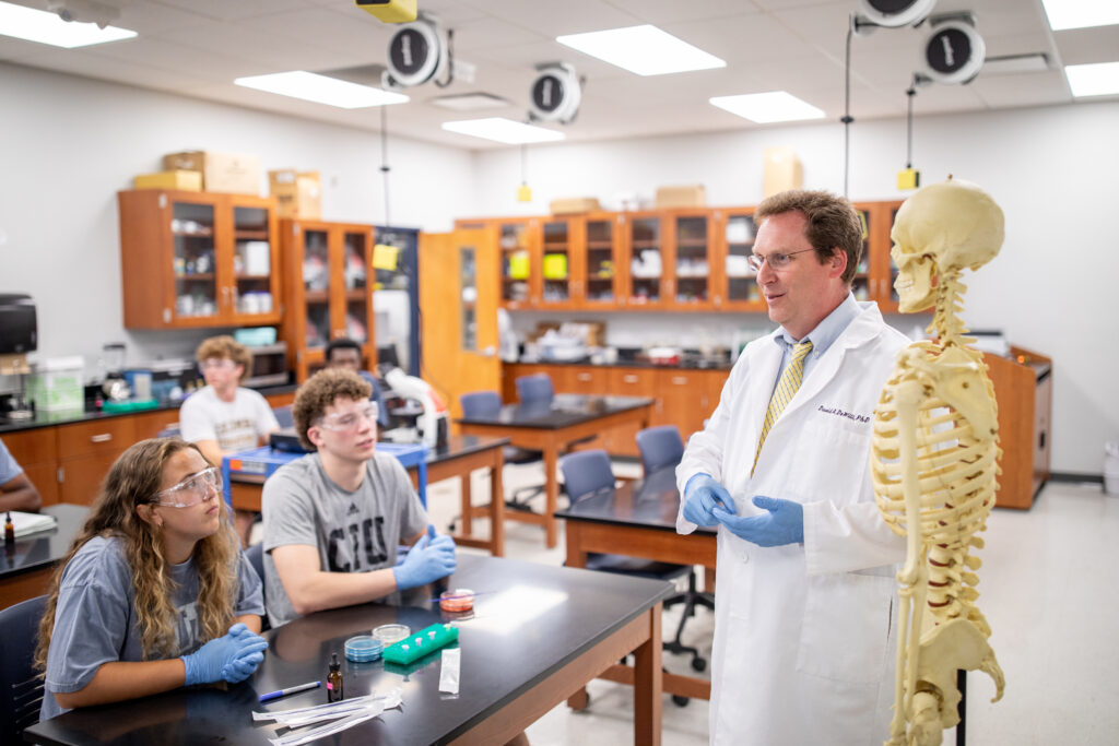 Dr. David DeWitt instructs students in a CIU science laboratory, standing beside an anatomical skeleton model