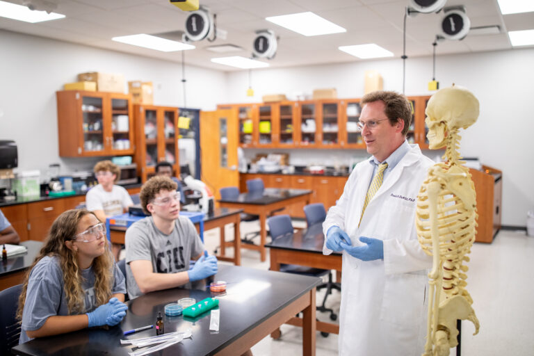 Dr. David DeWitt instructs students in a CIU science laboratory, standing beside an anatomical skeleton model
