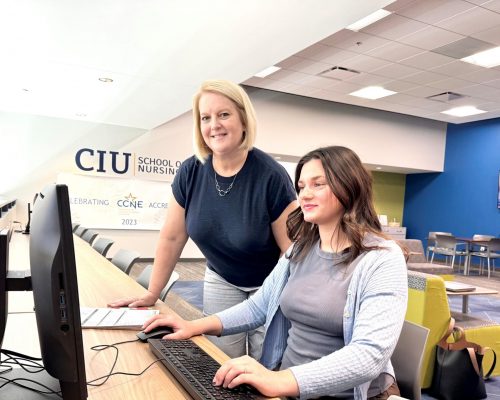 An academic advisor stands beside a student seated at a computer in the CIU School of Nursing building